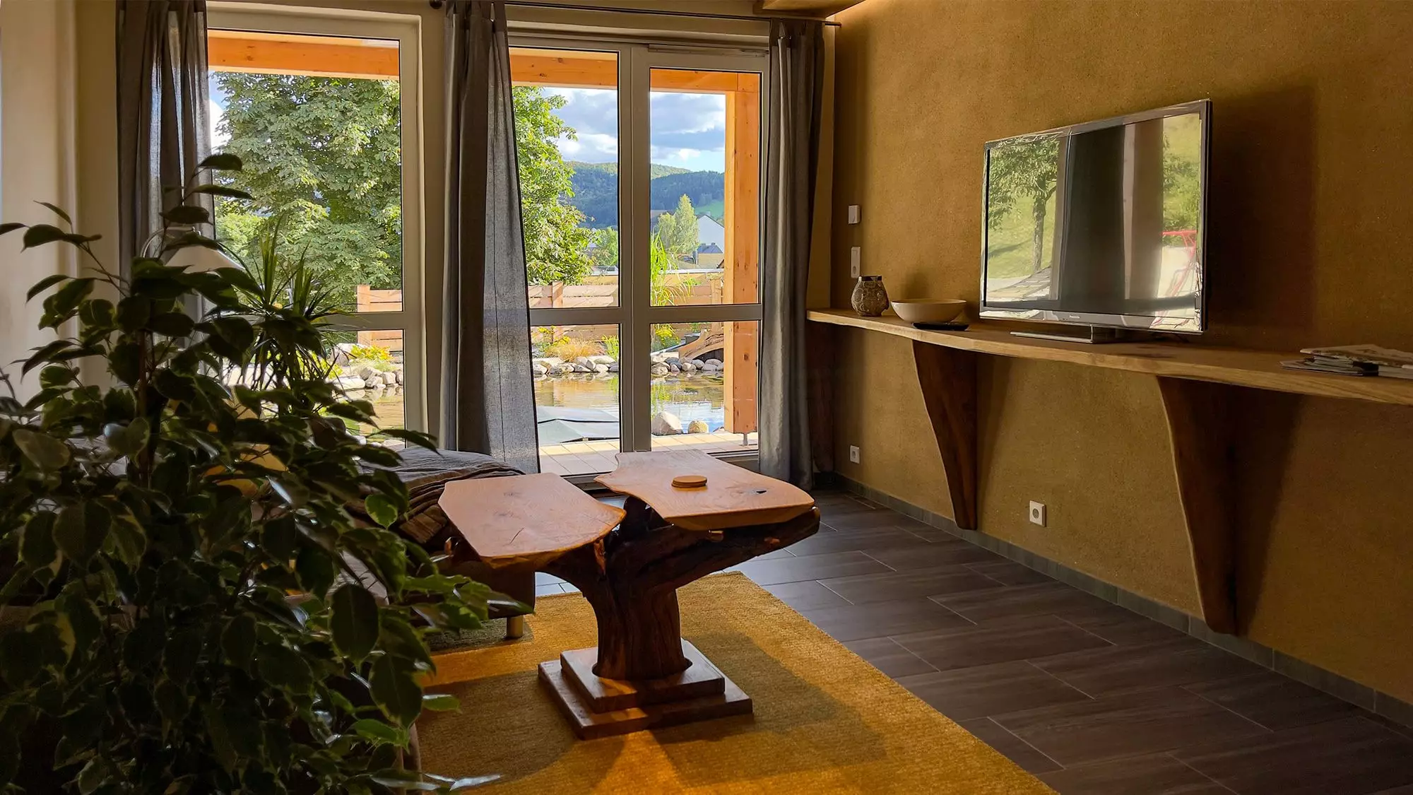 Wohnzimmer mit Holztisch und Smart TV mit Blick ins Grüne der Ferienwohnung Olbernhau